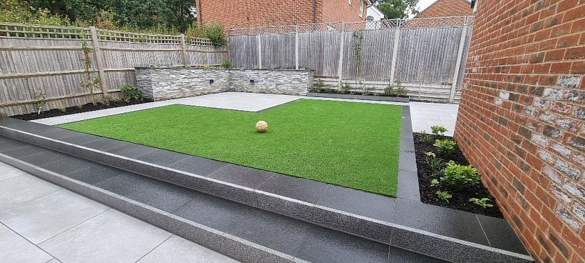 My latest landscaping project consisting of porcelain paving with granite steps & risers. Block planter with split-faced cladding, capped with granite. Artificial lawn and planting.
